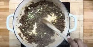 Cooking seasoned ground beef with onions in a white skillet.